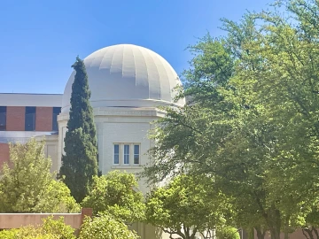 Steward Observatory framed by an array of diverse trees and shrubs.